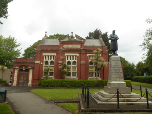 Single story red brick building, with statue of a man on a column in front of it.